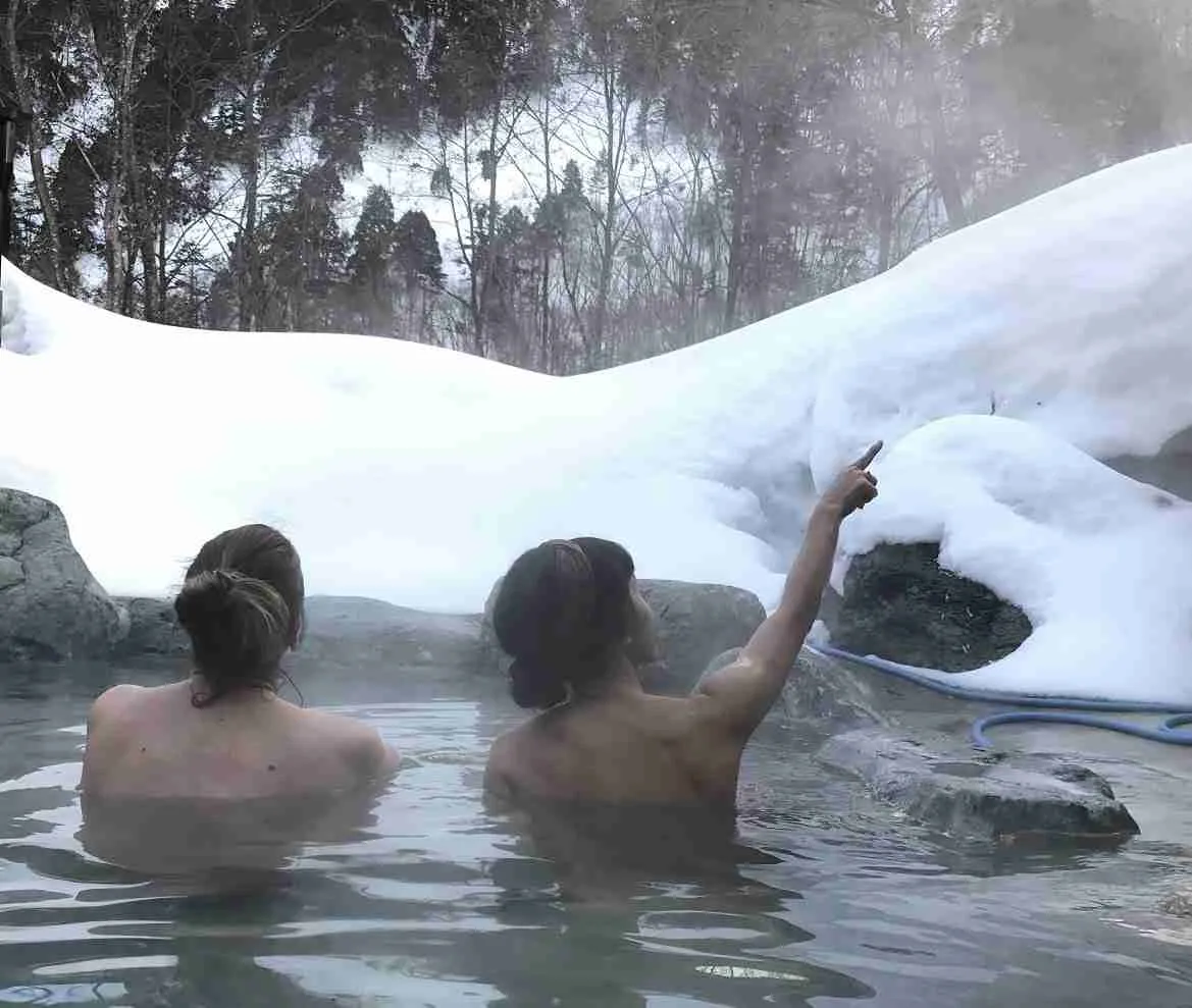 2 women bathing in Obinata No Yu Hakuba Onsen surrounded by snow