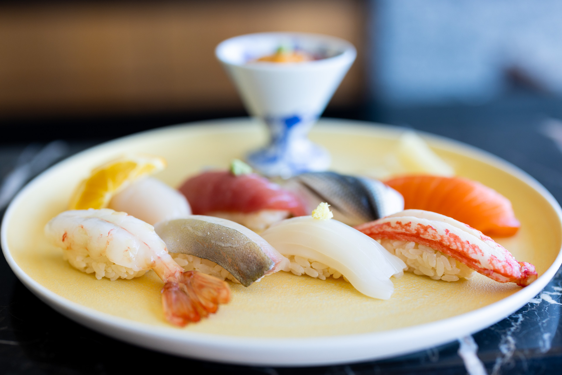 Elegant nigiri sushi platter with fresh prawn, tuna, squid, salmon and mackerel served on a yellow ceramic plate in Niseko