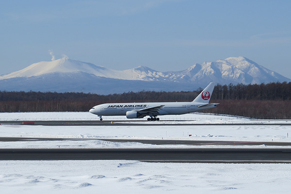 Japan Airlines plane on snowy runway at New Chitose Airport with Mount Yotei in background, Hokkaido winter scene
