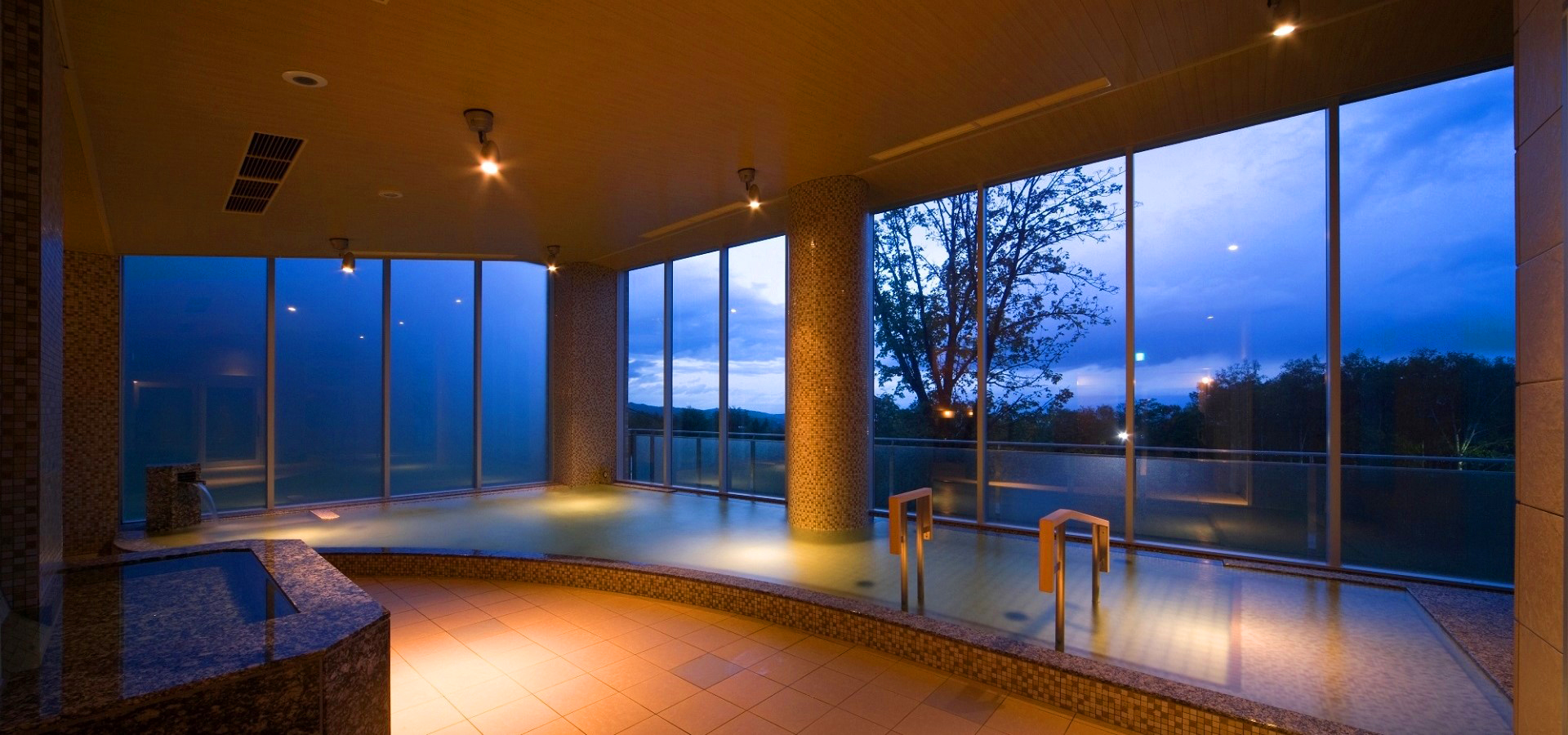 Indoor onsen at New Furano Prince Hotel with baths filled with water and a sunset view