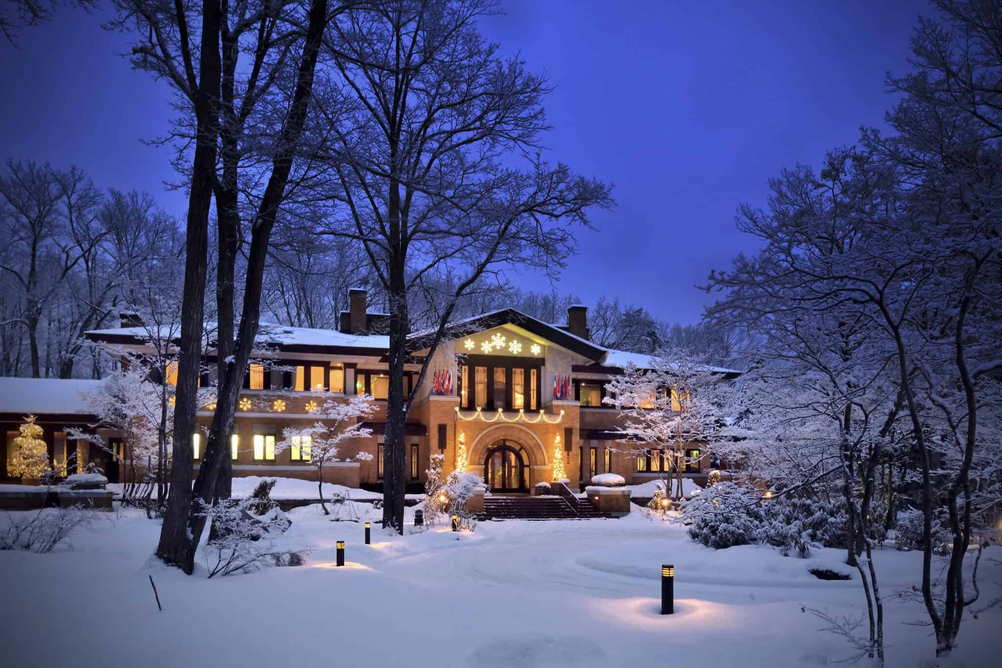 Snow-covered Hakuba accommodation at night with warm lights and winter trees.