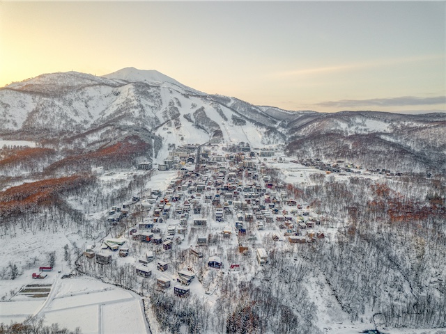 Aerial view of Hirafu Village in winter, nestled at the base of the snow-covered Niseko Grand Hirafu ski resort slopes.