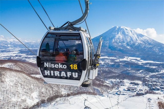 Niseko Hirafu gondola cabin carrying skiers up the mountain with a clear view of Mount Yotei under a bright blue sky.