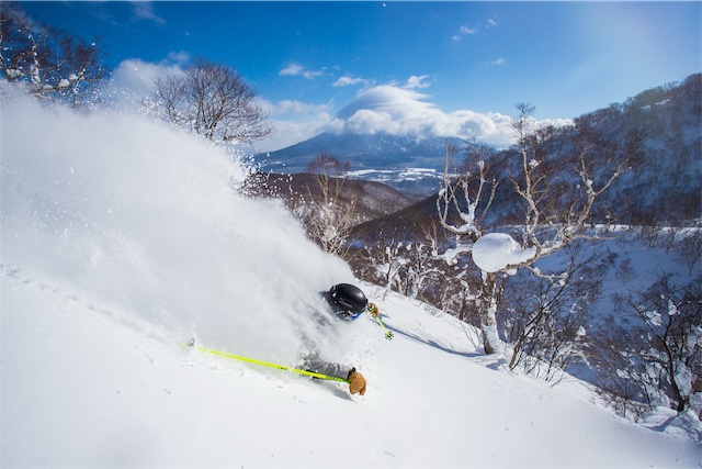 Skier carving through deep powder in Niseko with Mount Yotei in background, dynamic winter action in snowy Japanese landscape.