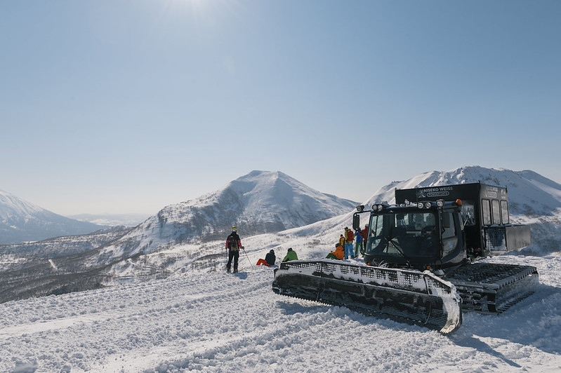 Niseko Weiss powder cat skiing group on a sunny alpine ridge with a snowcat and panoramic mountain views of Hokkaido