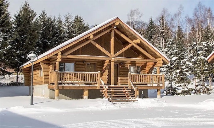 A traditional log cabin villa surrounded by snow and pine trees at Rusutsu Resort in winter.