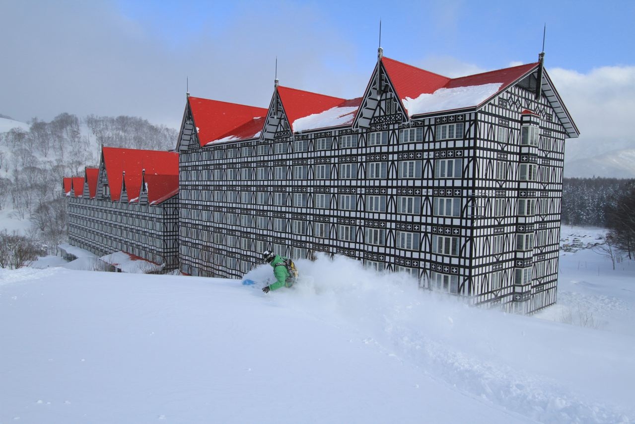 Skier in deep powder with the iconic Tudor-style Hotel Green Plaza Cortina and its red roofs in the background.