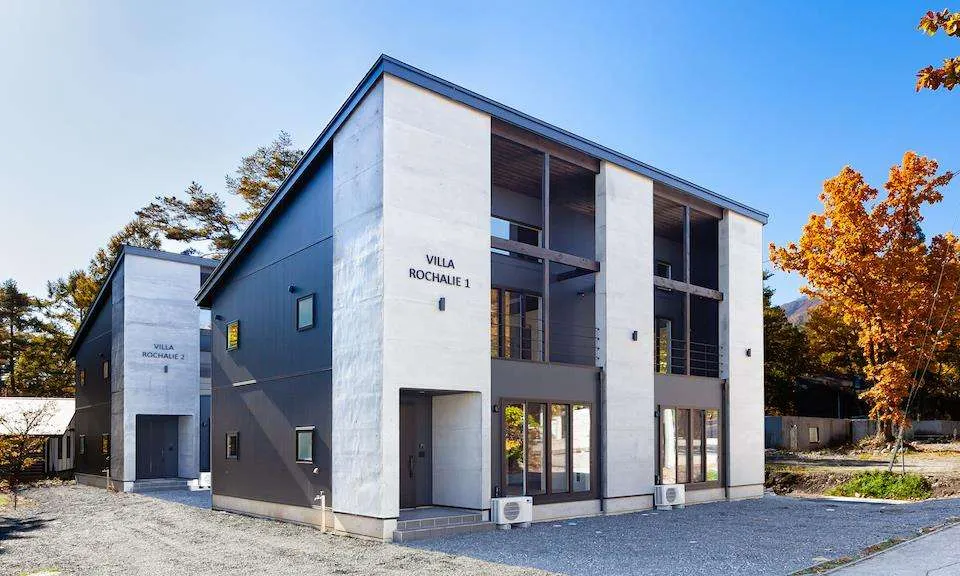 Pair of modern grey and white villas with large windows and flat roofs under a clear blue sky.