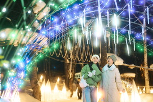 Two women walk under a tunnel of glowing blue and white icicle lights at Furano Kan Kan Mura.