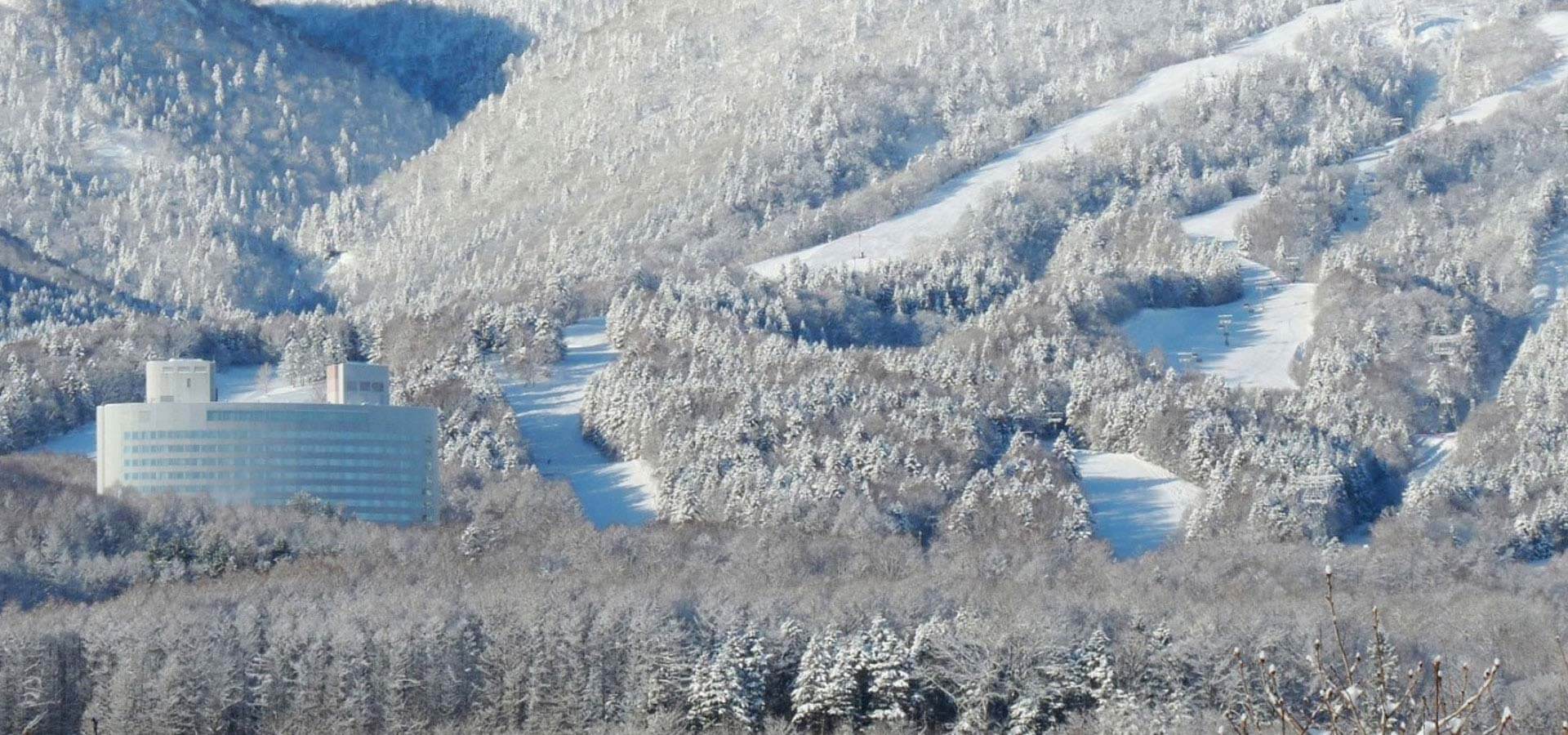 New Furano Prince Hotel beside snow-covered ski slopes and forested mountains in Furano, Hokkaido winter landscape