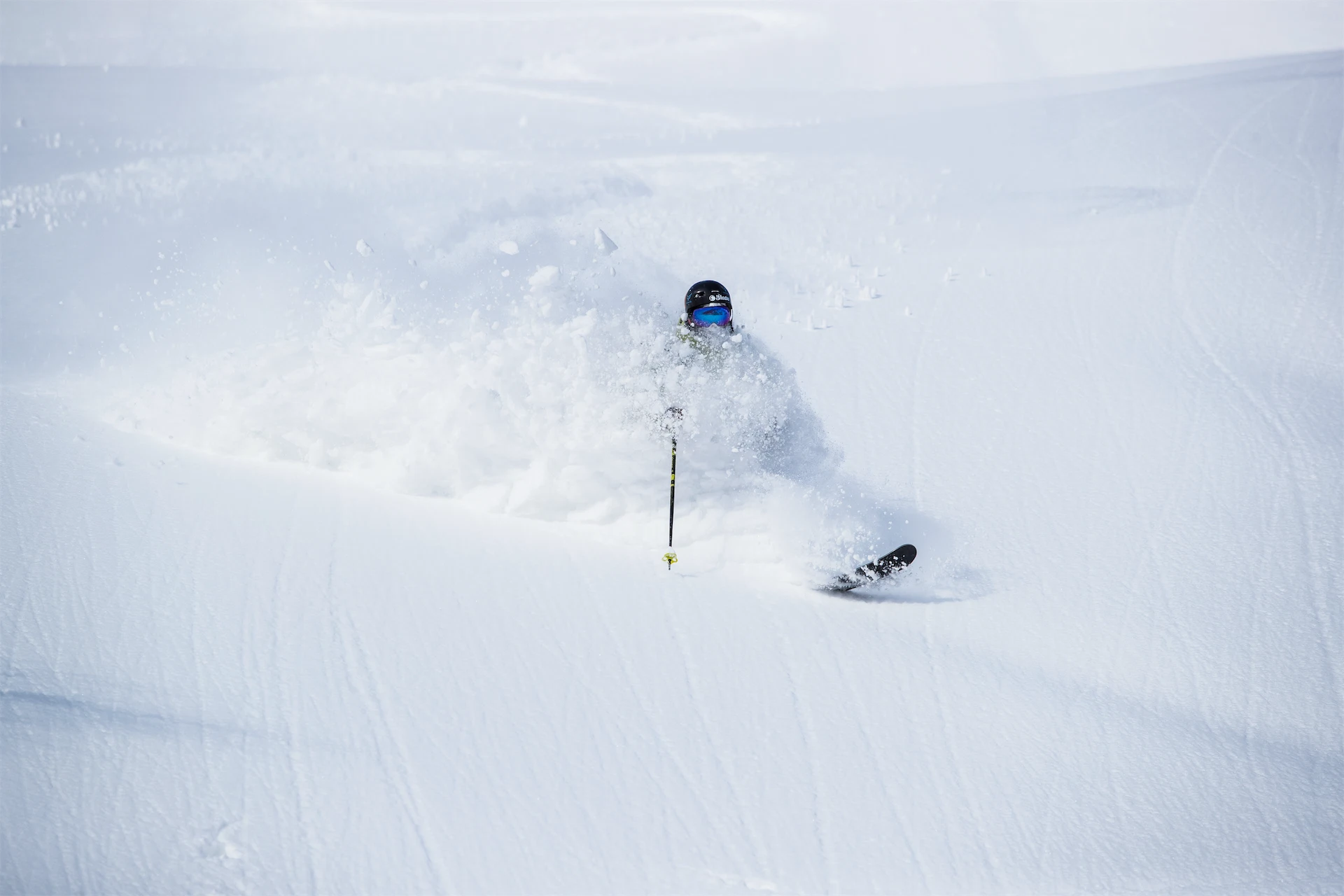 A skier disappears into a massive spray of deep white powder snow on a steep slope in Furano.