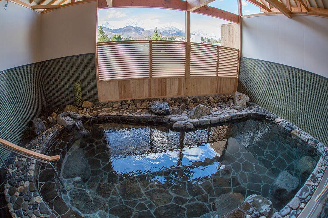 Steaming outdoor stone onsen bath in Hakuba with a scenic view of snow-capped mountains.