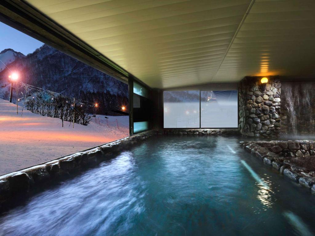 Indoor onsen at Hotel Green Plaza Hakuba overlooking illuminated snowy ski slopes at night.