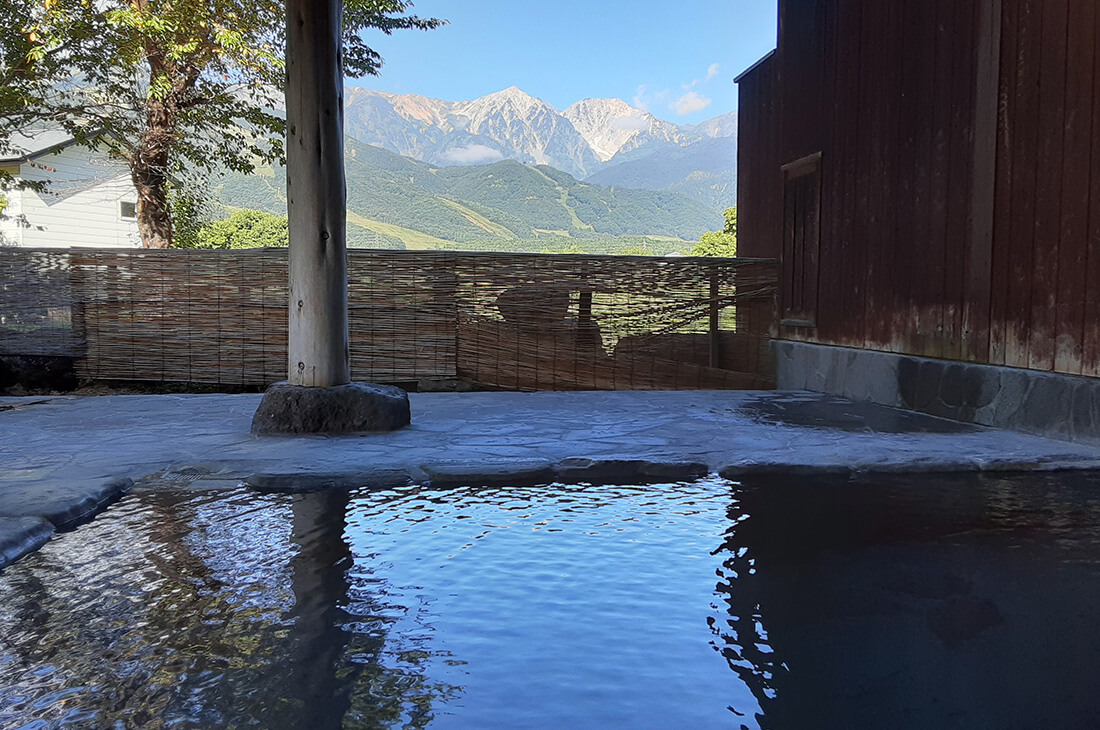 Traditional outdoor stone onsen bath with a panoramic view of the Hakuba mountain range.