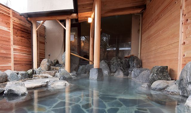 Traditional outdoor rock onsen bath featuring steaming thermal water and a wooden architectural frame.