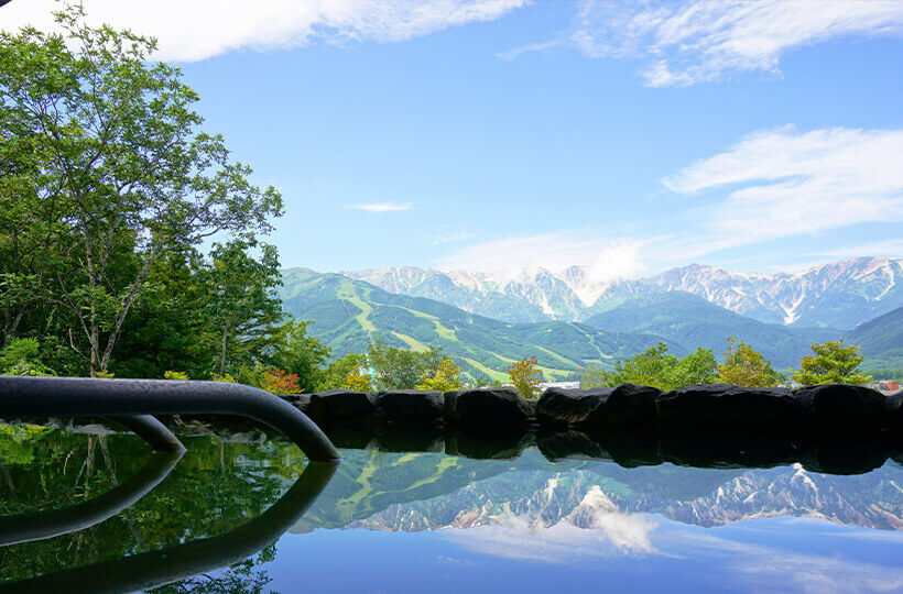 Scenic onsen bath reflecting the Northern Alps and blue sky in Hakuba, Japan.