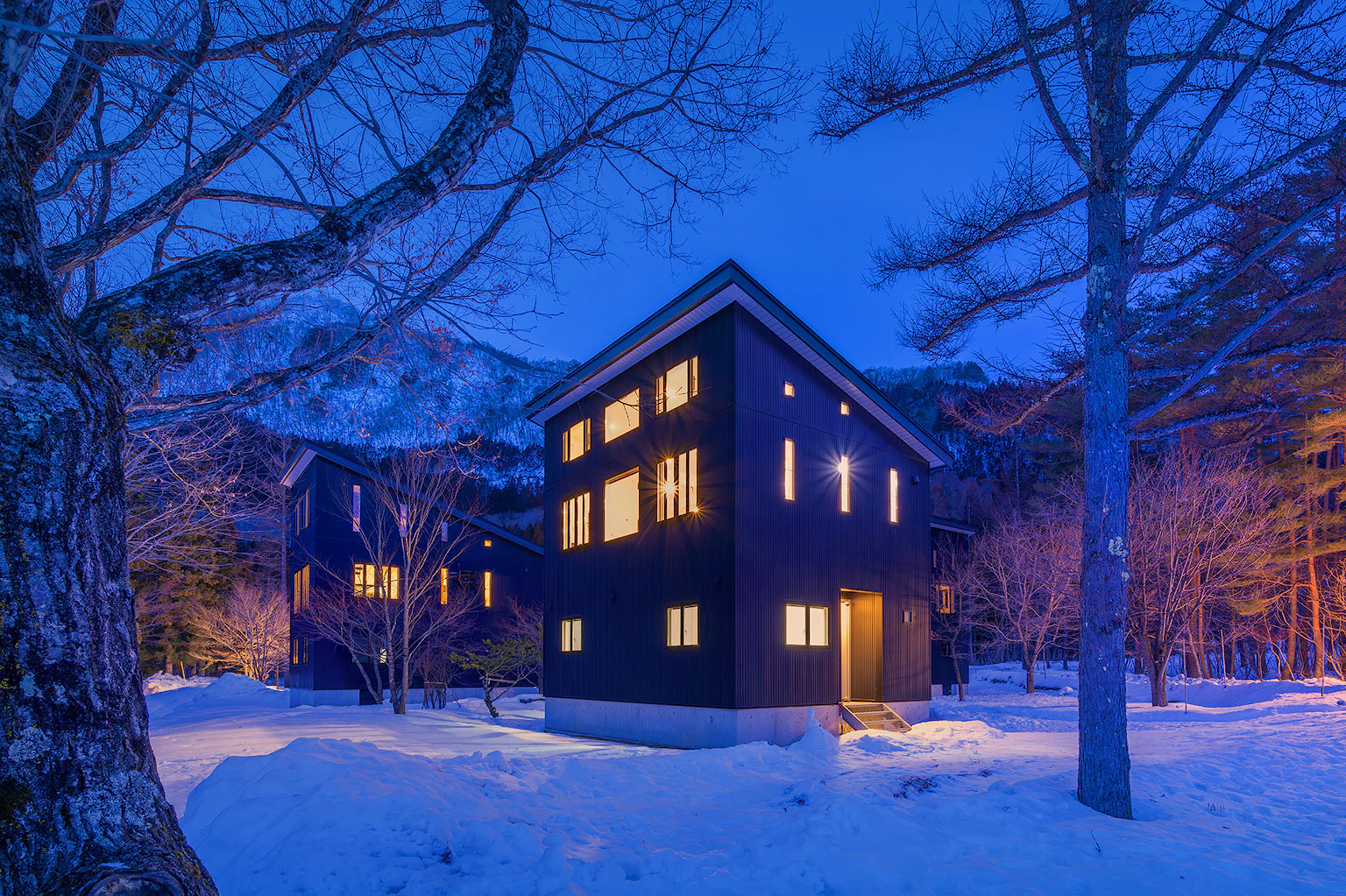 Three-story mountain lodge with balconies and a snow-covered roof at night.