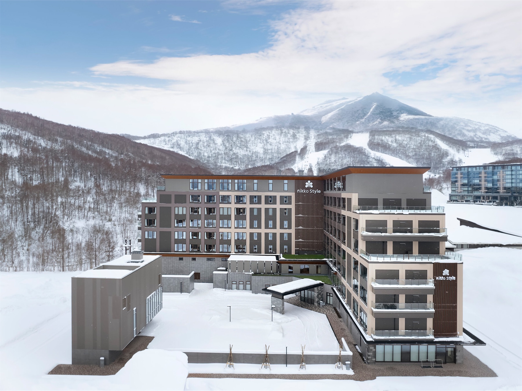 Modern Nikko Style hotel exterior in a snowy valley with ski runs and mountains in the background.