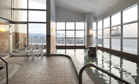 Bright indoor onsen with tiled floors and large windows looking out at a snowy landscape in Furano.