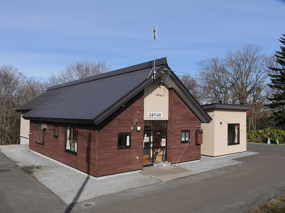 Exterior view of a traditional brown wooden public onsen building in Rusutsu under a clear blue sky.