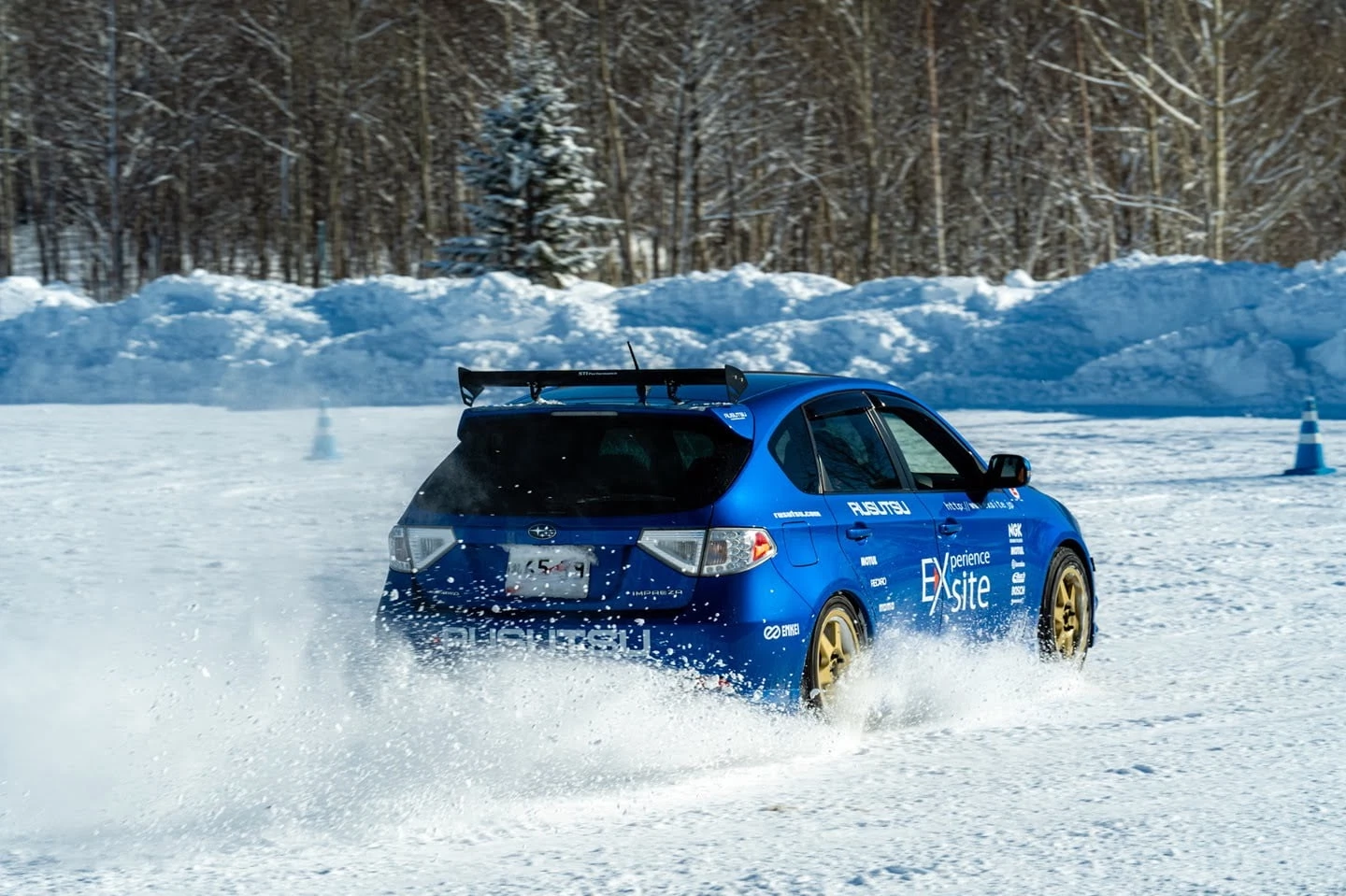 A blue rally car kicking up powder while drifting through a specialized snow course, featuring "Rusutsu" and "Experience" branding.