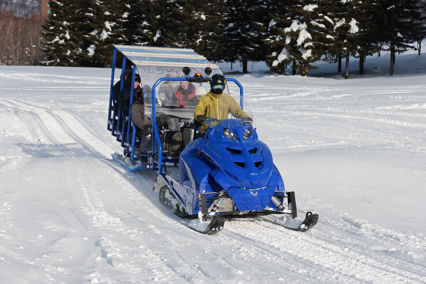 A snowmobile pulling a train of colorful passenger sleds across a snowy field in Rusutsu.