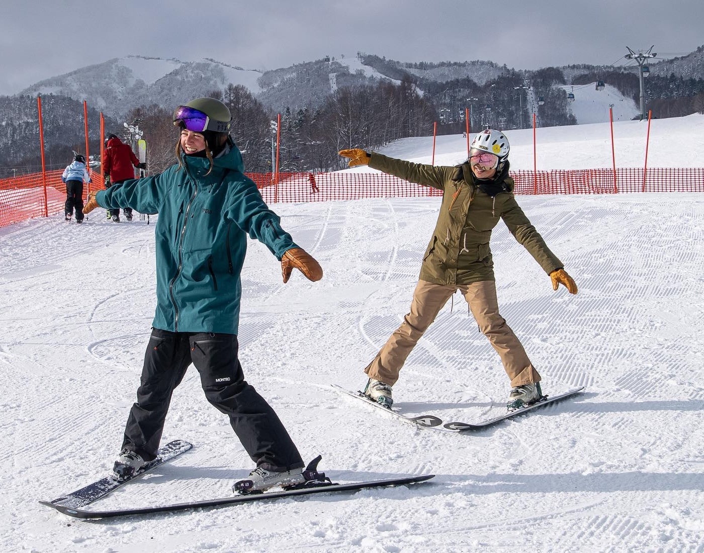 Two skiers in blue and tan jackets practicing balance and form on a snowy slope.