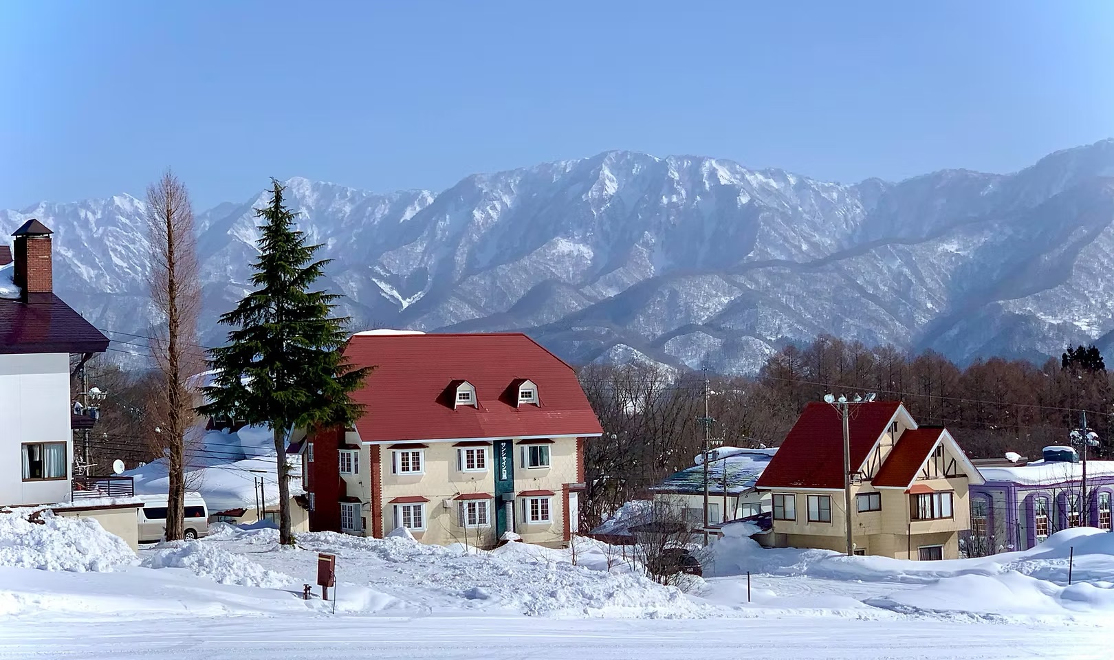 Red-roofed mountain chalets in a snowy valley with towering snow-capped peaks in the background.