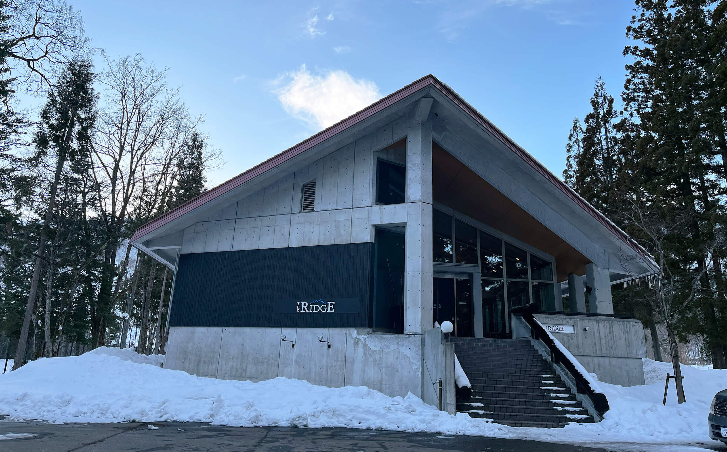 Minimalist concrete ski lodge architecture featuring "The Ridge" signage and a wide staircase in the snow.