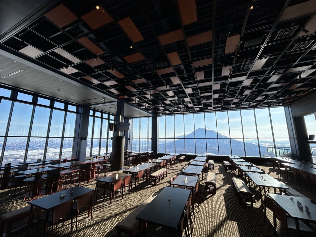 A wide-angle interior view of a modern restaurant in Niseko, Japan, looking out at Mount Yotei.