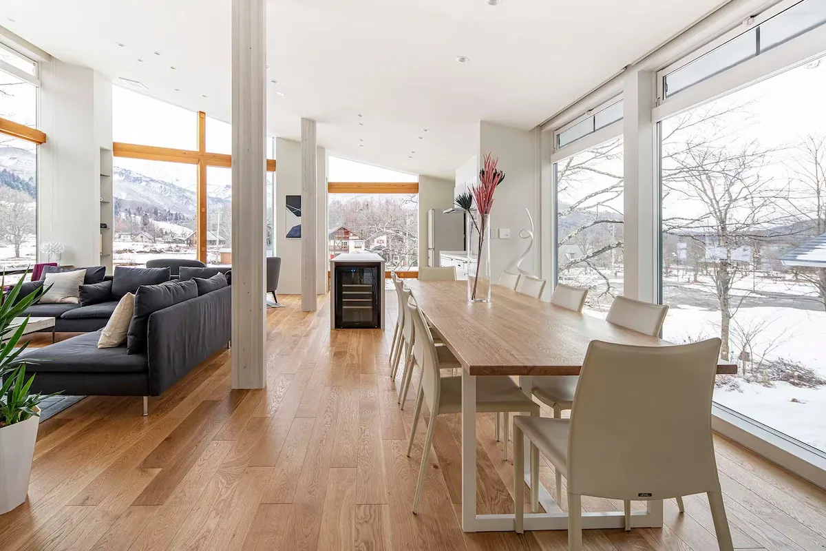 Modern open-plan living and dining area with floor-to-ceiling windows overlooking snowy mountains.