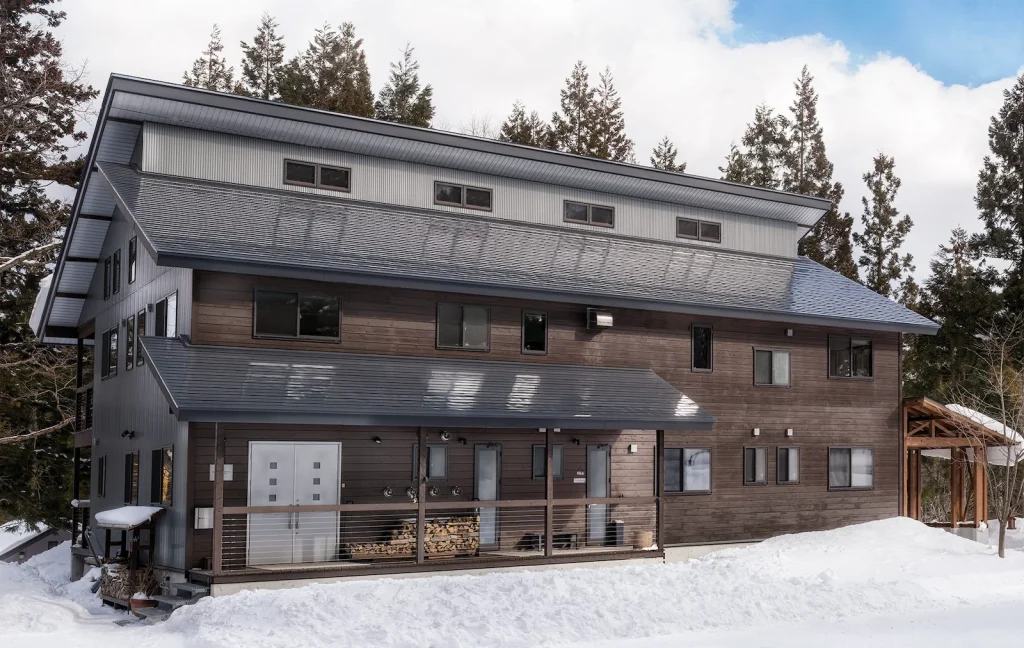 Exterior of a large dark wood mountain lodge with a metal roof surrounded by deep winter snow.