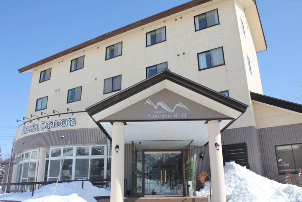 Exterior of Hakuba Panorama Hotel and Taproom entrance with snow banks on a sunny day.