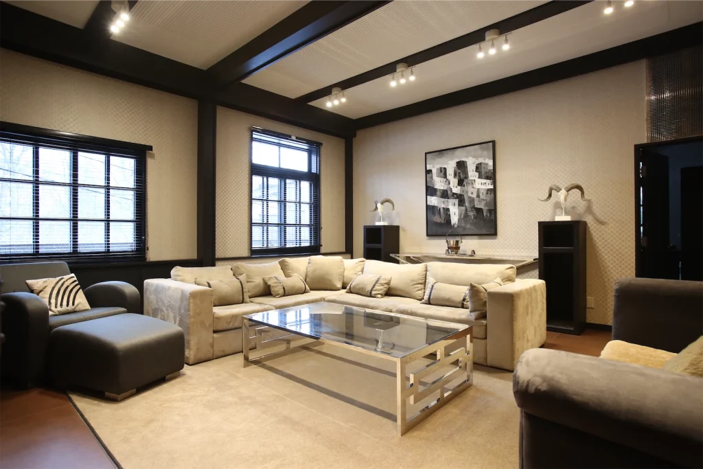 Elegant lounge featuring a large beige sectional sofa, glass coffee table, and dark wood ceiling beams.