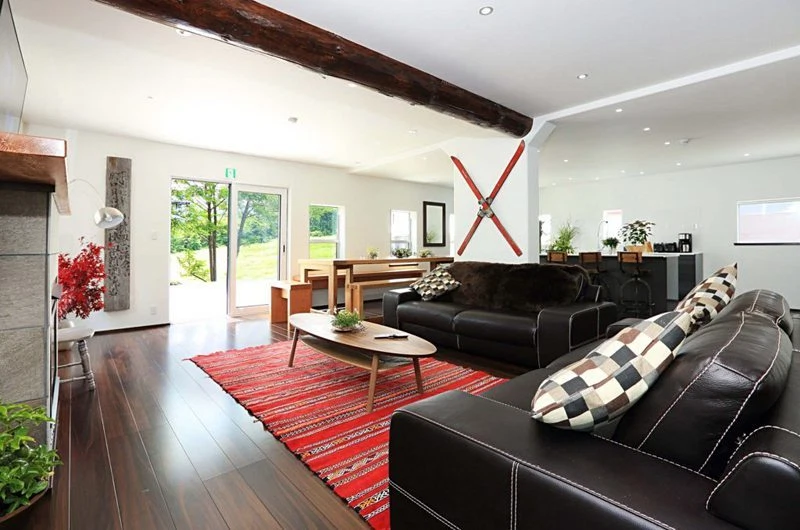Spacious living room with dark leather sofas, red patterned rug, rustic ceiling beam, and ski decor.