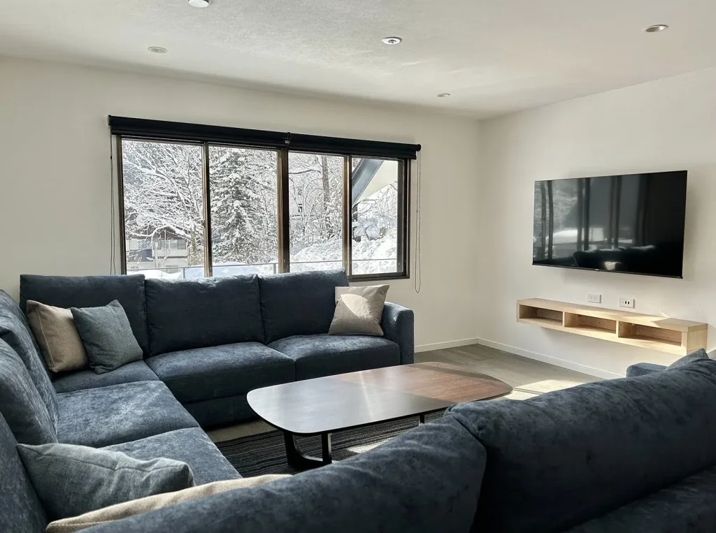 Modern living room featuring a plush blue sectional sofa, wall-mounted TV, and snowy window views.