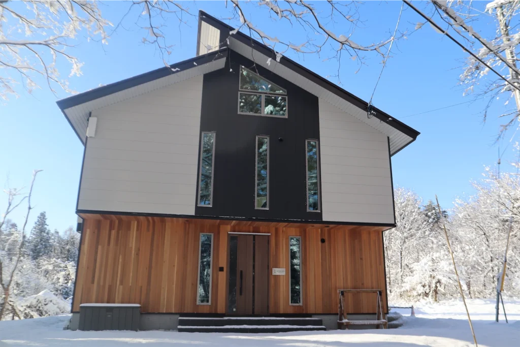 Modern Hokujo chalet featuring wood paneling and black-and-white facade in a snowy setting.