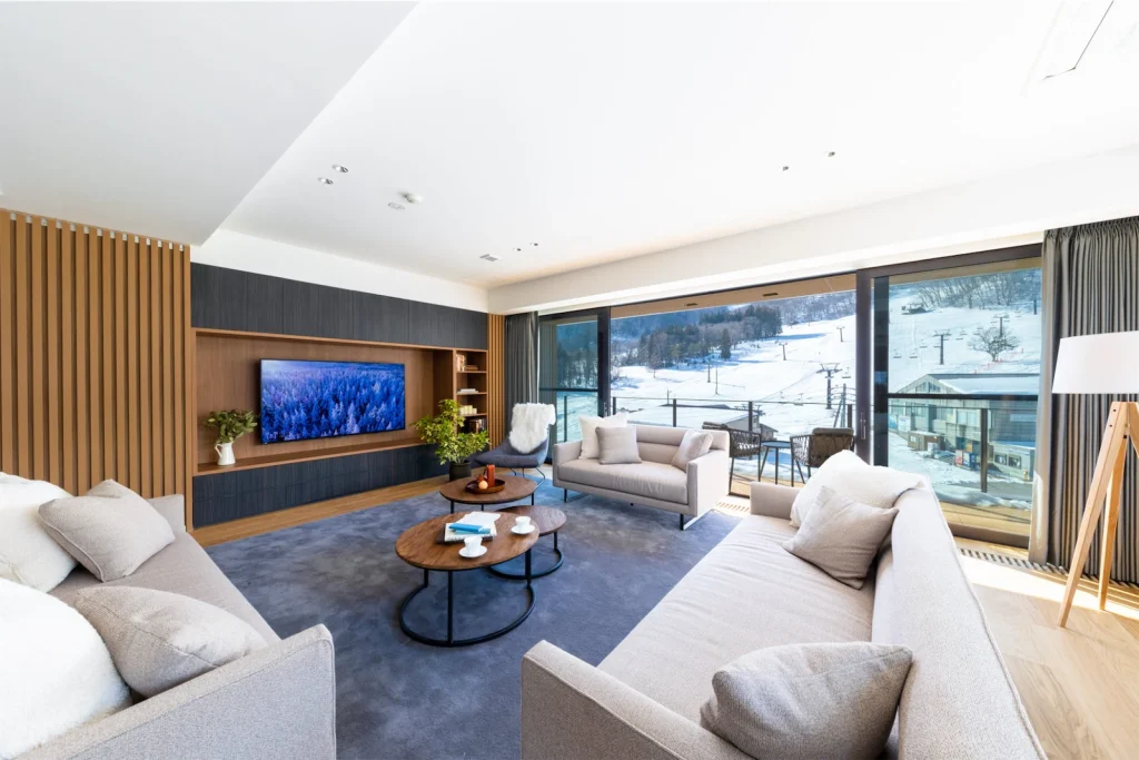 Contemporary living room with grey sofas, a large TV, and a balcony overlooking snowy ski slopes.