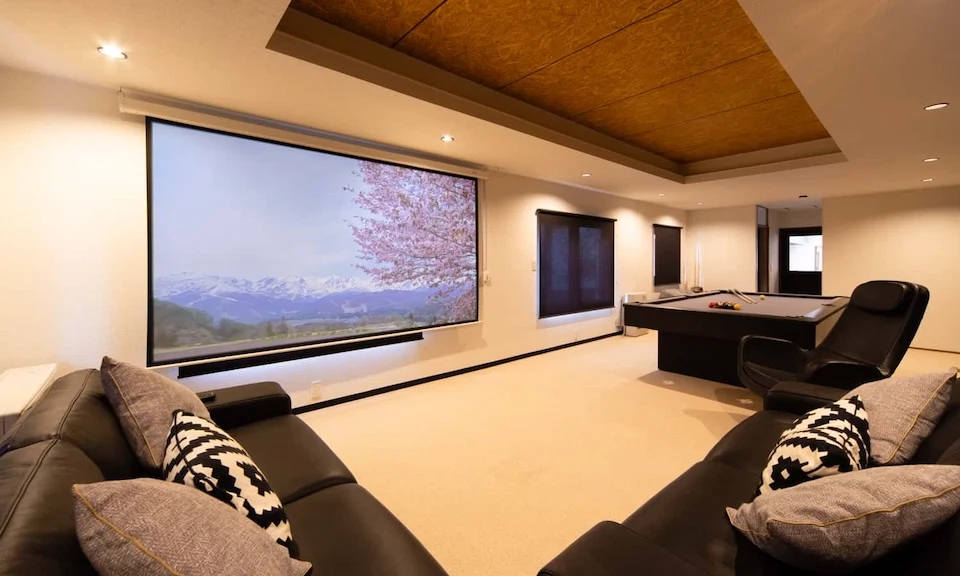 Entertainment room featuring a massive projector screen, black leather sofas, and a modern pool table.