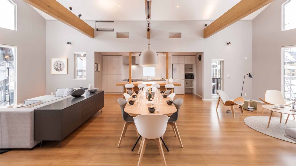 Open-plan living space featuring high ceilings, wooden beams, and a long formal dining table.