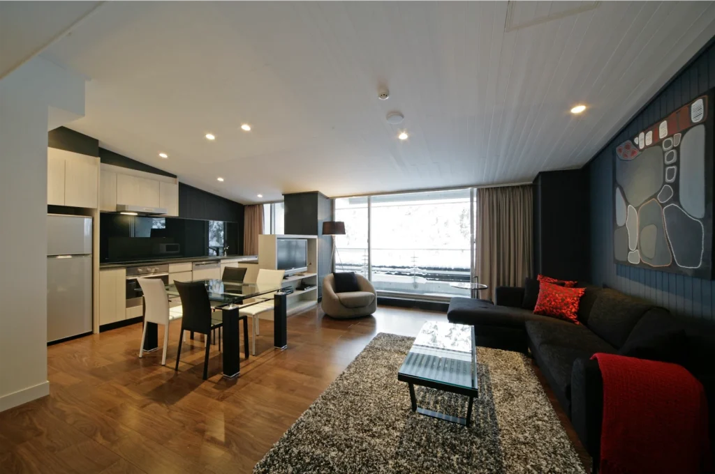 Modern open-plan apartment featuring a sleek kitchen, glass dining table, and dark living area.