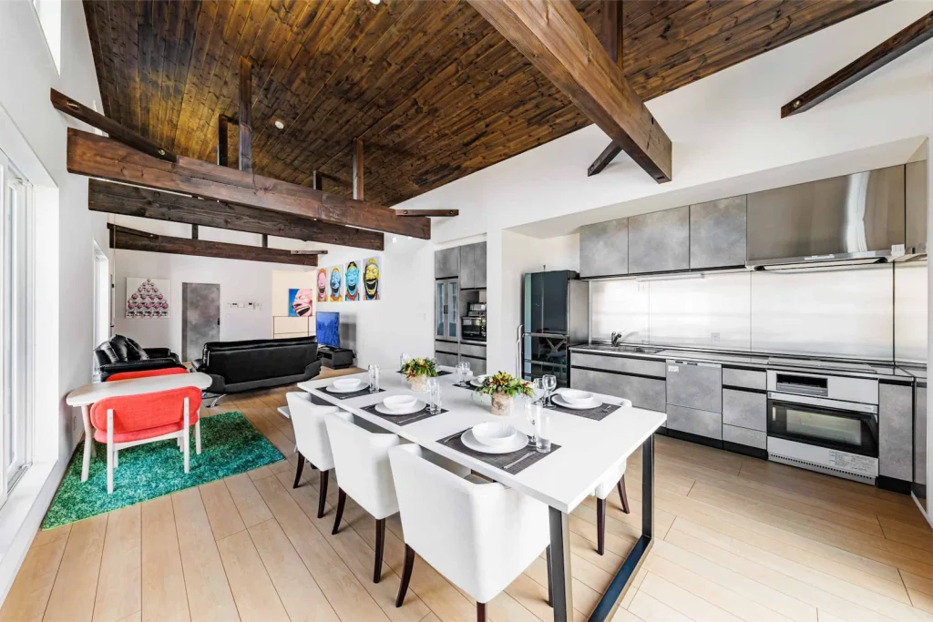 Open kitchen and dining area with modern grey cabinets, a white table, and rustic wood ceiling beams.