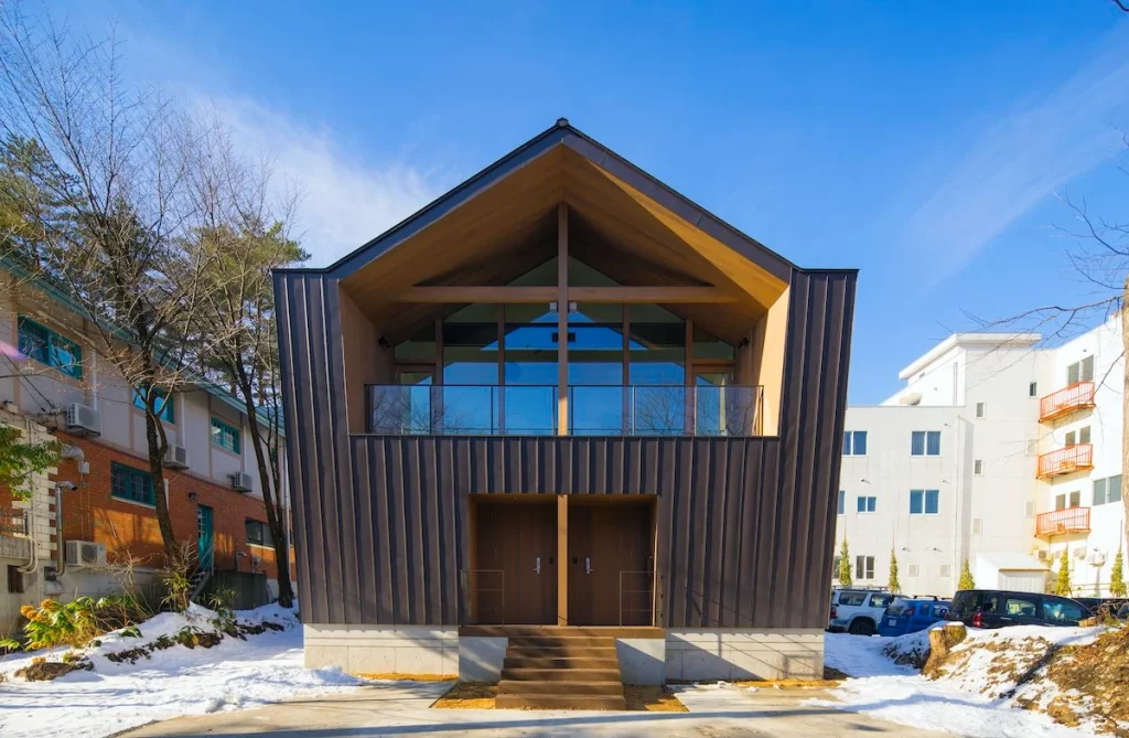 Modern symmetrical A-frame chalet by White Fox with dark metal siding and wood accents.