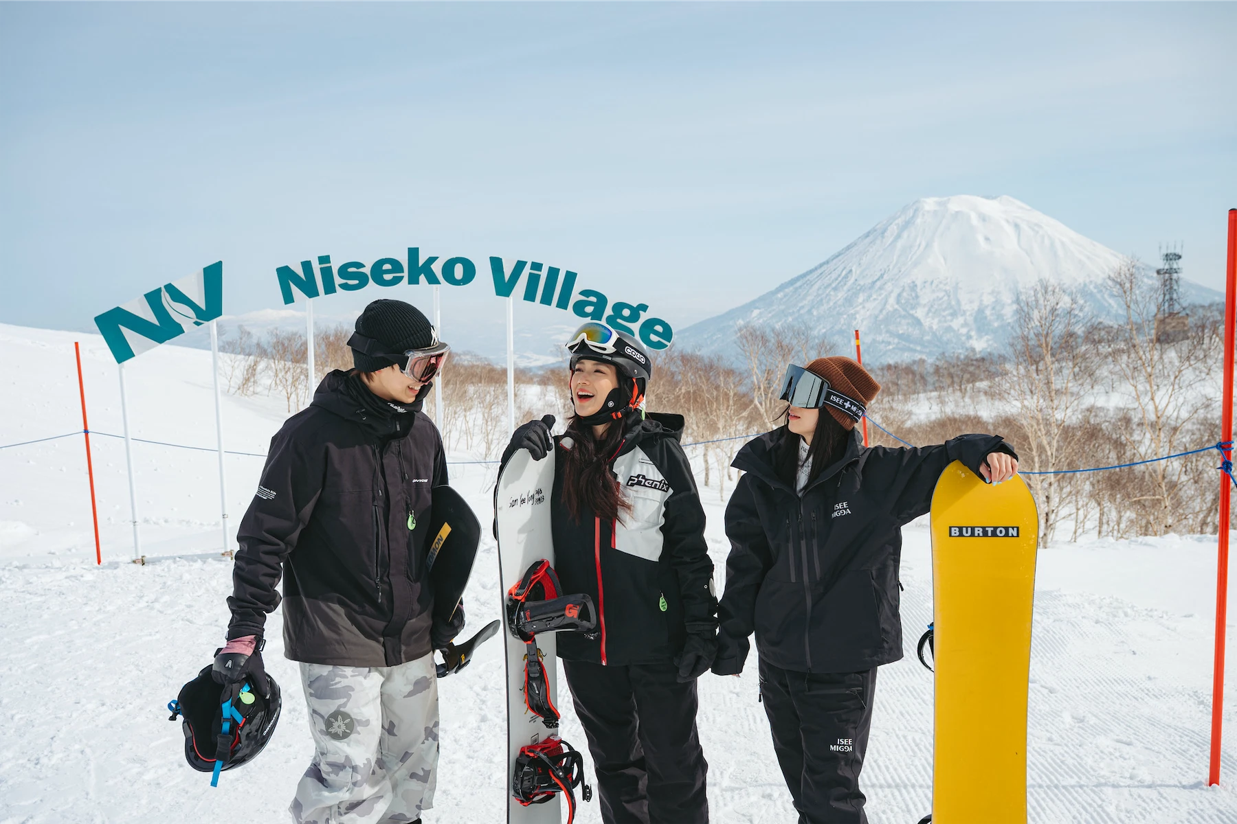 Three snowboarders posing by the Niseko Village sign with Mount Yotei in the background, Japan.