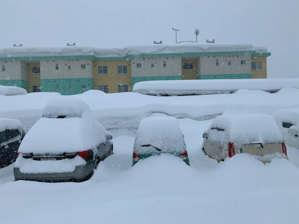 Cars buried in heavy snow in a residential parking lot during a winter snowstorm.