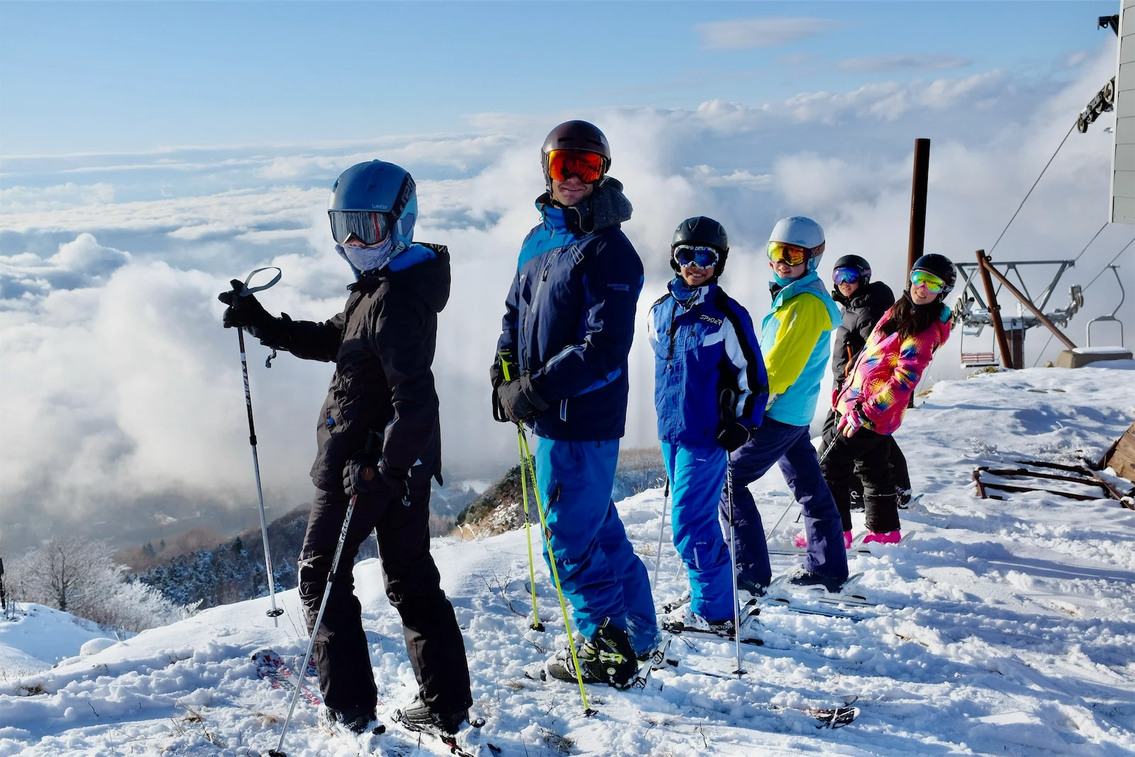 IMG_0032.webp - Group of skiers standing in a line along a snowy mountain ridge with a sea of clouds behind them.
