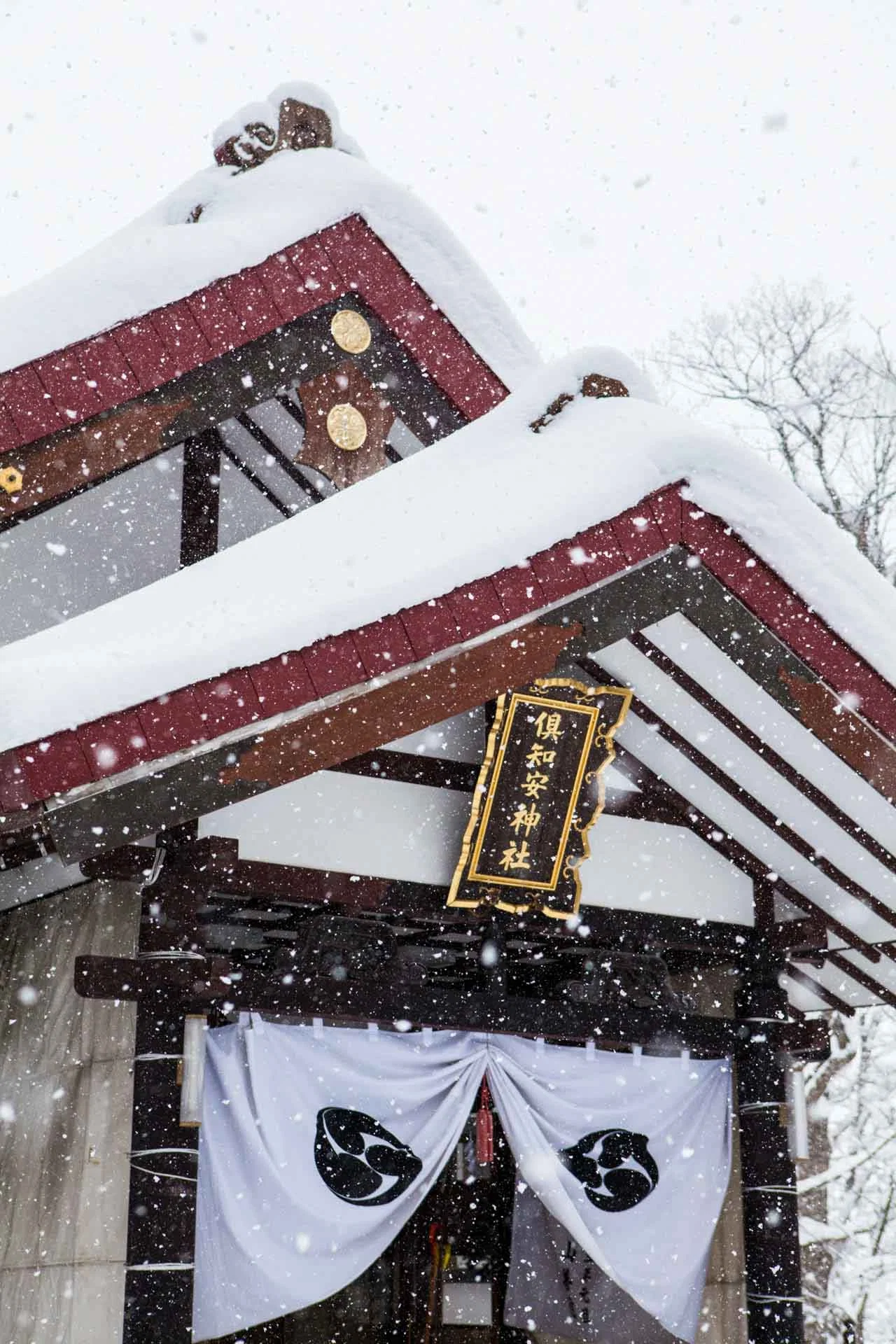 Snow-laden roof and sign of Kutchan Shrine during a winter snowfall.