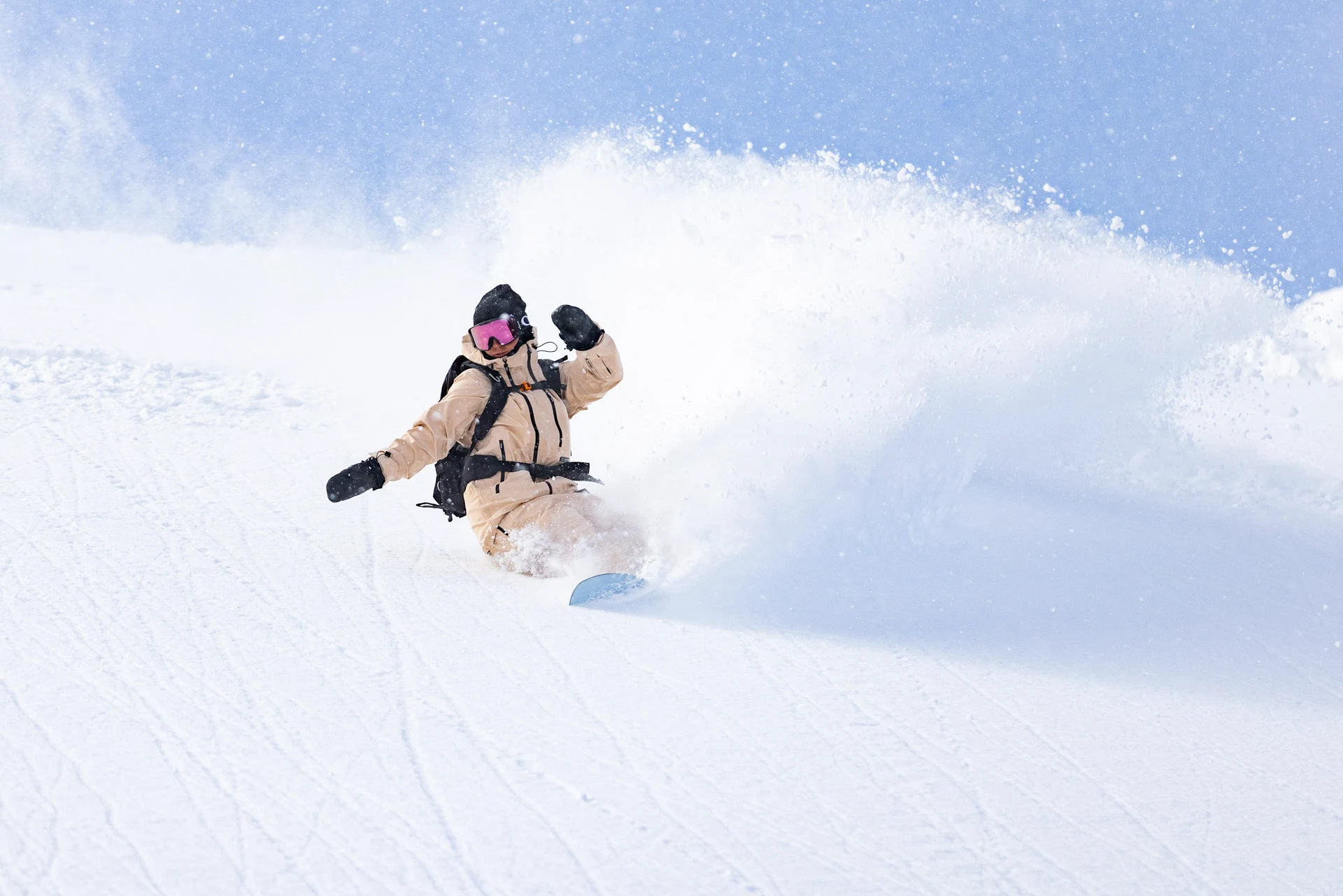 Snowboarder in a beige snowsuit carving a sharp turn through powder snow.
