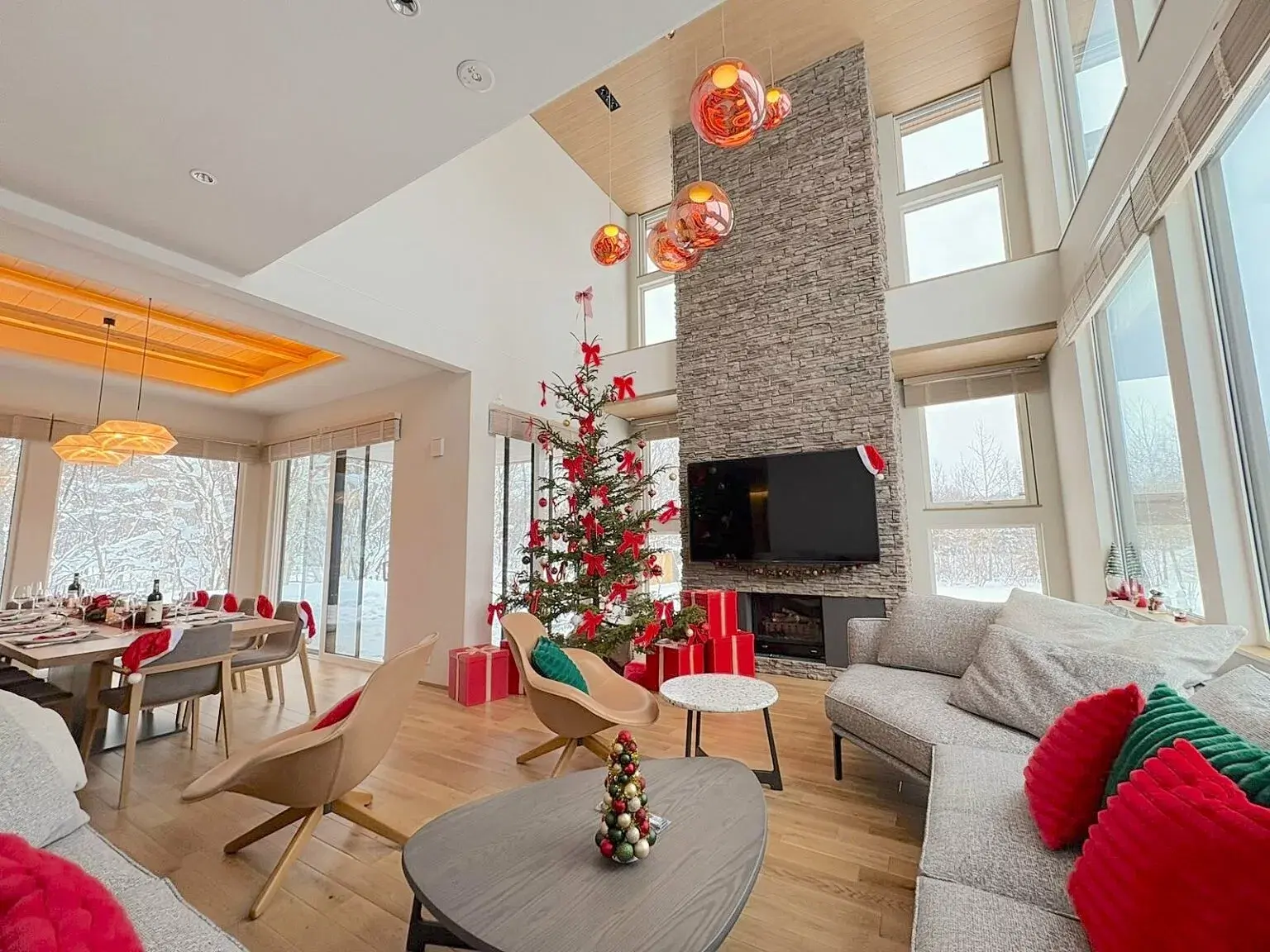 Festive chalet living room with double-height ceilings, a stone fireplace, and a decorated Christmas tree.